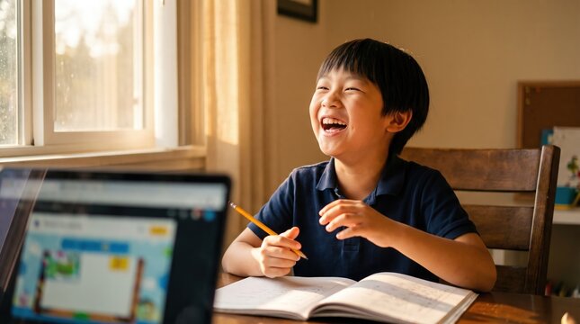 Cheerful Asian boy laughing during home study with notebook and laptop for elementary education and distance learning advertisement