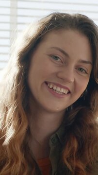 Vertical video: Smiling woman reacting to camera cue, laughing at window blinds, button-up shirt
