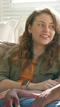 Vertical video: Hearing partner's joke, woman in olive shirt smiling laughing touching arm on couch