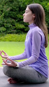 Vertical video: Settling woman meditating for calm on deck with mat, purple top, smartwatch