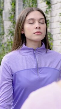 Vertical video: Noticing off-right person, woman purple zip top opening eyes, smiling in courtyard