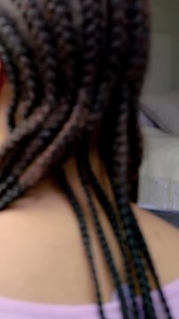 Vertical video: Stepping woman in pink top turning into bedroom, revealing hoop earring and braids