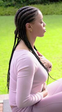 Vertical video: Inhaling woman in pink gear breathing with hands on chest and belly on mat for calm