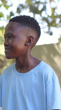 Vertical video: Smiling boy laughing and gesturing near pale wall under trees, light-blue T-shirt