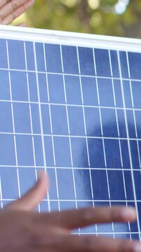 Vertical video: Reaching bare arms sliding and steadying PV panel under trees to mount
