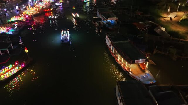 Vibrant boats with colorful lights navigate the river at night in Hoi An, Vietnam, creating a lively and festive scene along the waterway