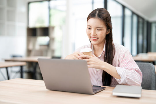 Happy Asian woman working on laptop in modern office.