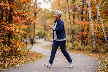 Obraz premium Senior woman power walking on a path in a beautiful autumn park