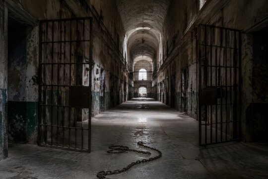 An empty prison corridor with open iron doors and chains on the floor.