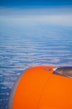 Airplane engine flying above striped clouds in blue sky