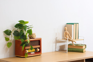 Vintage radio with a green plant, wooden mannequin, and old books on a light wooden desk against a white wall © Pixel-Shot