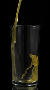 Pouring juice into the glass. Closeup on black background. Vertical footage