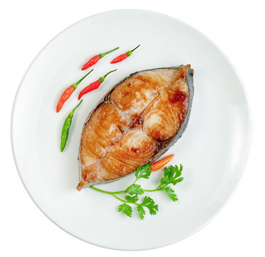 Fried king mackerel fish steak served on a white ceramic plate with fresh red chili peppers and coriander garnish Isolated. Top view of a healthy and tasty seafood meal.