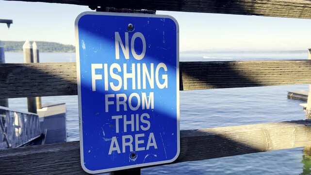 Blue no fishing sign on a wooden pier near the water. Waterfront safety notice, restricted area, outdoor public space.