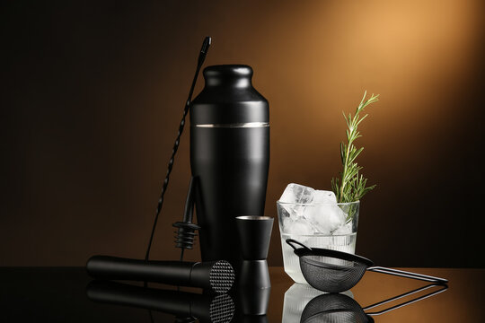 Bartender utensils and glass with cocktail on black table near brown wall, closeup