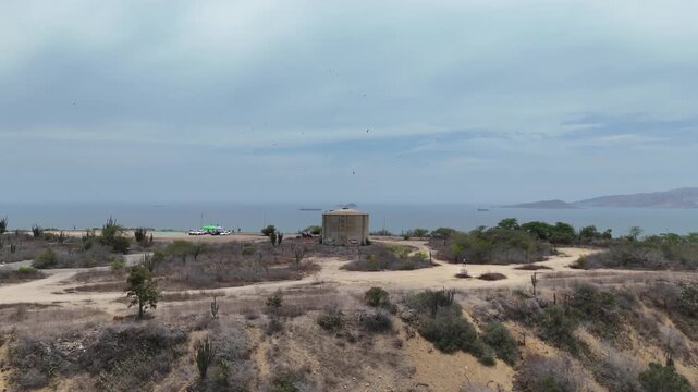 Drone shot ascending over an arid coastal hill to reveal a vast ocean view with cargo ships.