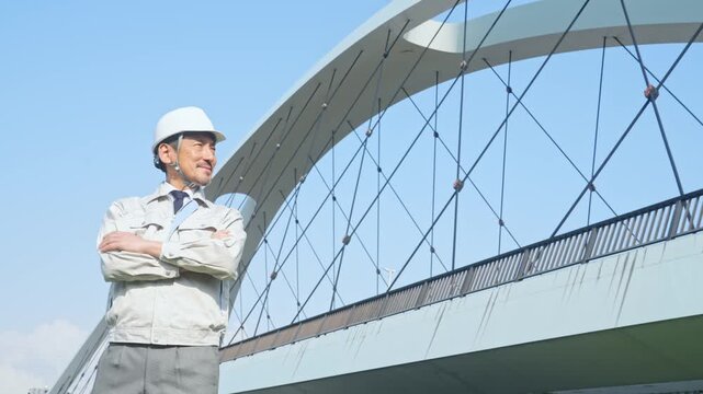 橋の前で遠くを眺める男性作業員。建設、工事、インフラ、点検、検査、メンテナンス、保守、安全、修理