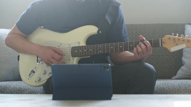 タブレットを見ながらエレキギターを弾く男性。音楽、楽器、演奏、練習、趣味、動画、バンド、音楽家、作曲