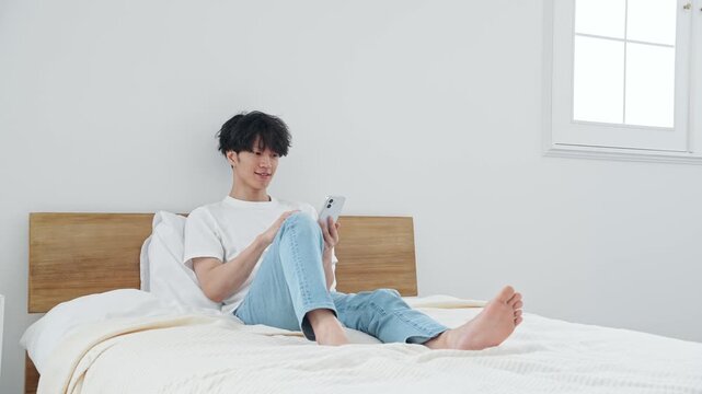 寝室でスマホを使う男性。アプリ、SNS、動画、リラックス、ベッド、ゲーム、笑顔、検索、AI、DX