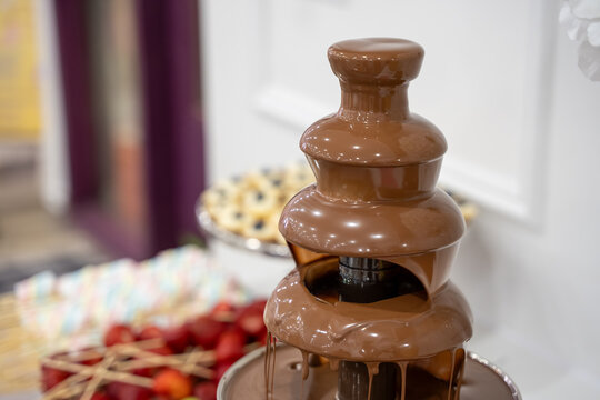 Close up of flowing chocolate fountain with dessert table.