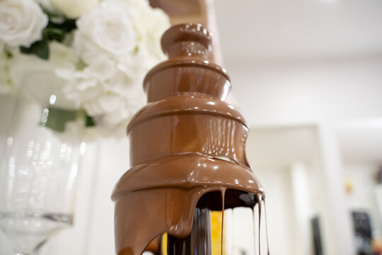 Close up of flowing chocolate fountain beside white flowers.