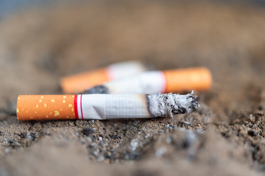 Closeup of burning cigarette butt resting dusty ground ash shallow depth of field highlighting smoking addiction pollution public health concerns