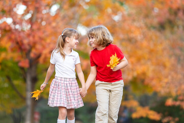 Fototapeta premium Autumn foliage behind children. Autumn background near child. Joyful autumn kids play. Cute autumn friends walk.