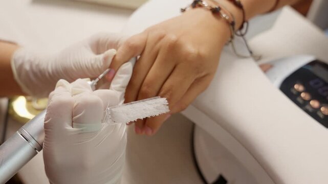 Manicurist shaping nails with electric file during professional manicure