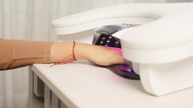 Woman drying nail polish in uv lamp at beauty salon