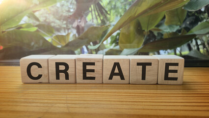 Create wooden blocks spelling word CREATE with green foliage background symbolizing creativity inspiration concept © Jen