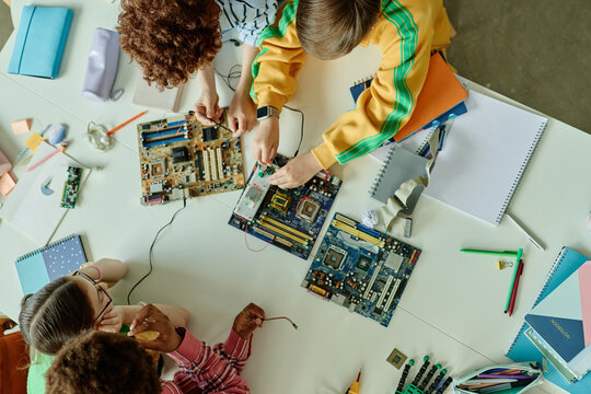 Overhead shot of diverse teenagers assembling computer circuit boards and testing electronics during classroom workshop, supporting STEM education, coding camp, maker program marketing