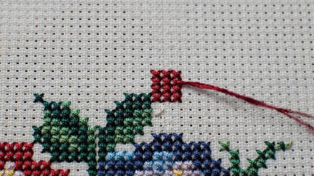 Close-up of a hand cross-stitching on white fabric showcasing the needlework art of embroidery
