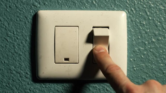 Close up view of hand turning on light switch, white outlet plate against turquoise wall