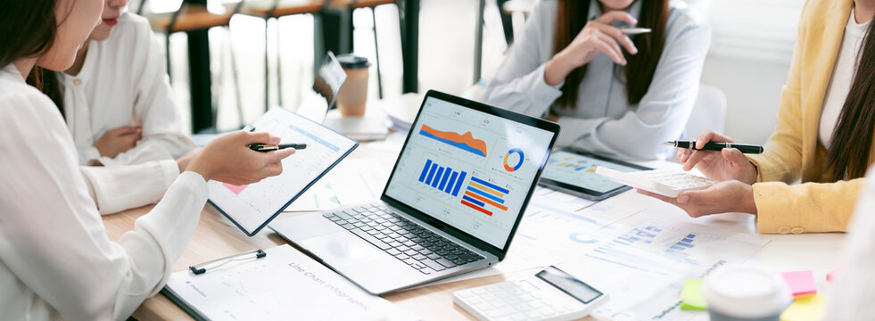 Business team analyzing financial charts on laptop in meeting, website banner format.