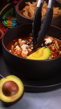 Mexican food, close up of person adding strips of pasilla chilli to prepare a Mexican tortilla soup, culinary preparation