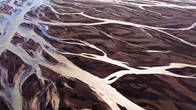 A stunning top-down aerial perspective capturing the intricate, vein-like patterns of a braided glacial river flowing through the dark volcanic landscape of Iceland.