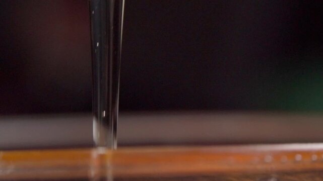 Macro view of honey stretching into thin stream as it drizzles downward, highlighting viscosity, golden color, smooth texture, and natural food characteristics