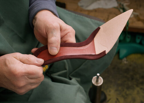 Footwear craft. Diy manufacturing. Unrecognizable professional cobbler man hands working with leather material sole at workspace.