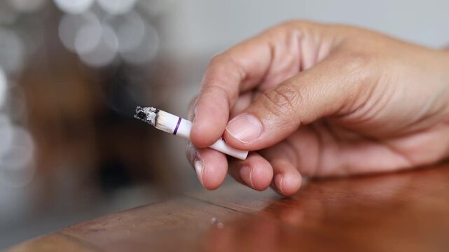 Close up of a hand holding a lit cigarette, symbolizing bad habits and nicotine addiction.