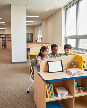 Vertical view of students using computers and tablets together during a collaborative digital learning lesson at school, with guided support and bright ambient light