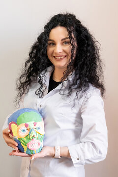 Anatomy teaching. Beauty expert. Smiling female professional cosmetologist in white uniform with colorful head in salon.