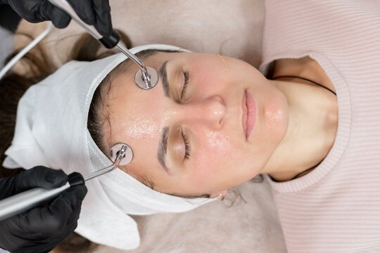 Microcurrent facial. Woman treatment. Cosmetologist hands in black gloves using professional device for lifting skin procedure.