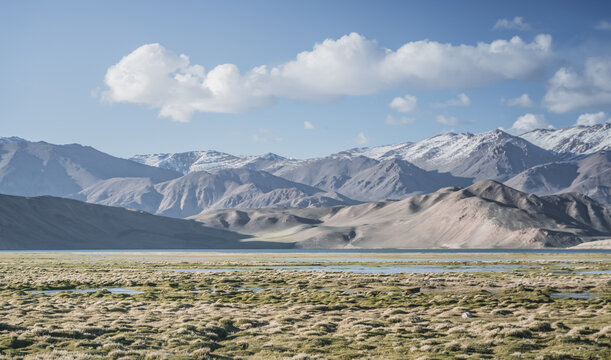 Clear-water rivers and lakes in a mountain valley, pastures and green grassy fields set against mountain ranges and snow-capped, glacier-clad peaks&mdash;a scenic landscape background