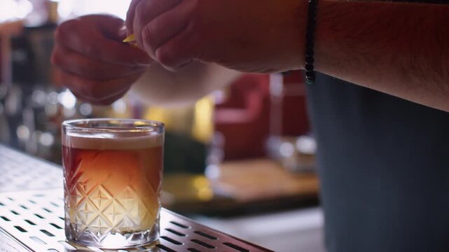 Cool drink. Classic beverage. Unrecognizable bartender man hands serving crystal glass garnished with lemon spiral zest red cherry on bar counter.