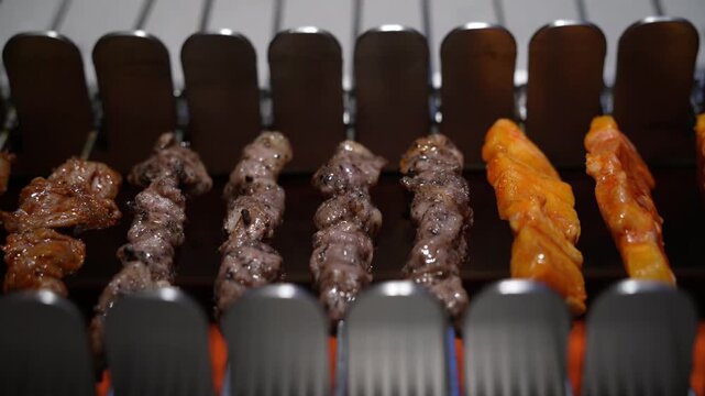 Auto Turning Skewers, BBQ Cooking Automation - Pork Meat on Skewers Roasted on Live Coals Automatically Spun With an Electric Machine For Even Roast in Korean Restaurant