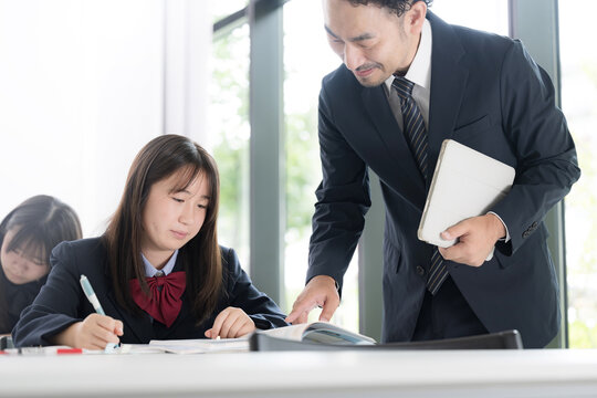 塾や学校の教室で個別指導を行う教師と勉強に取り組む日本人女子中学生や女子高校生　予備校や高校の授業風景　集団や個別塾などのイメージ上半身