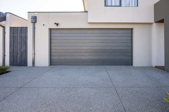 Exterior of a modern residential garage with horizontal panel sectional door. A spacious exposed aggregate concrete driveway in suburban Australia.