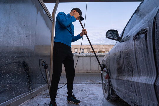 After sunset dark time Concept of vehicle maintenance, car care, cleanliness transportation and modern automated washing services. Man Washing Car at Self Service Car Wash Using Foam Cleaning System