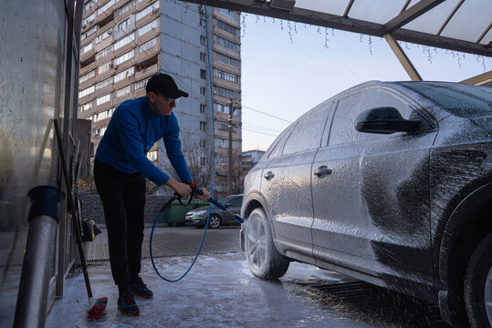 After sunset dark time Concept of vehicle maintenance, car care, cleanliness transportation and modern automated washing services. Man Washing Car at Self Service Car Wash Using Foam Cleaning System