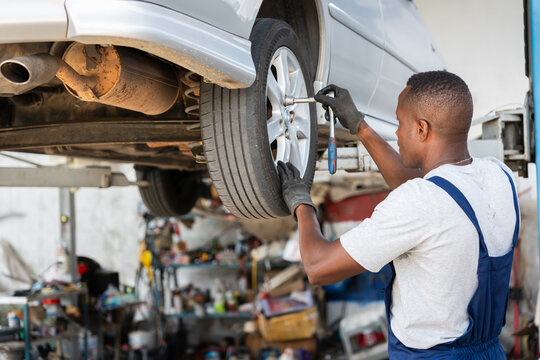 Car repair service professional replacing vehicle tire on lift, Professional auto technician using wrench to remove wheel at garage, African American mechanic changing car tire in auto workshop